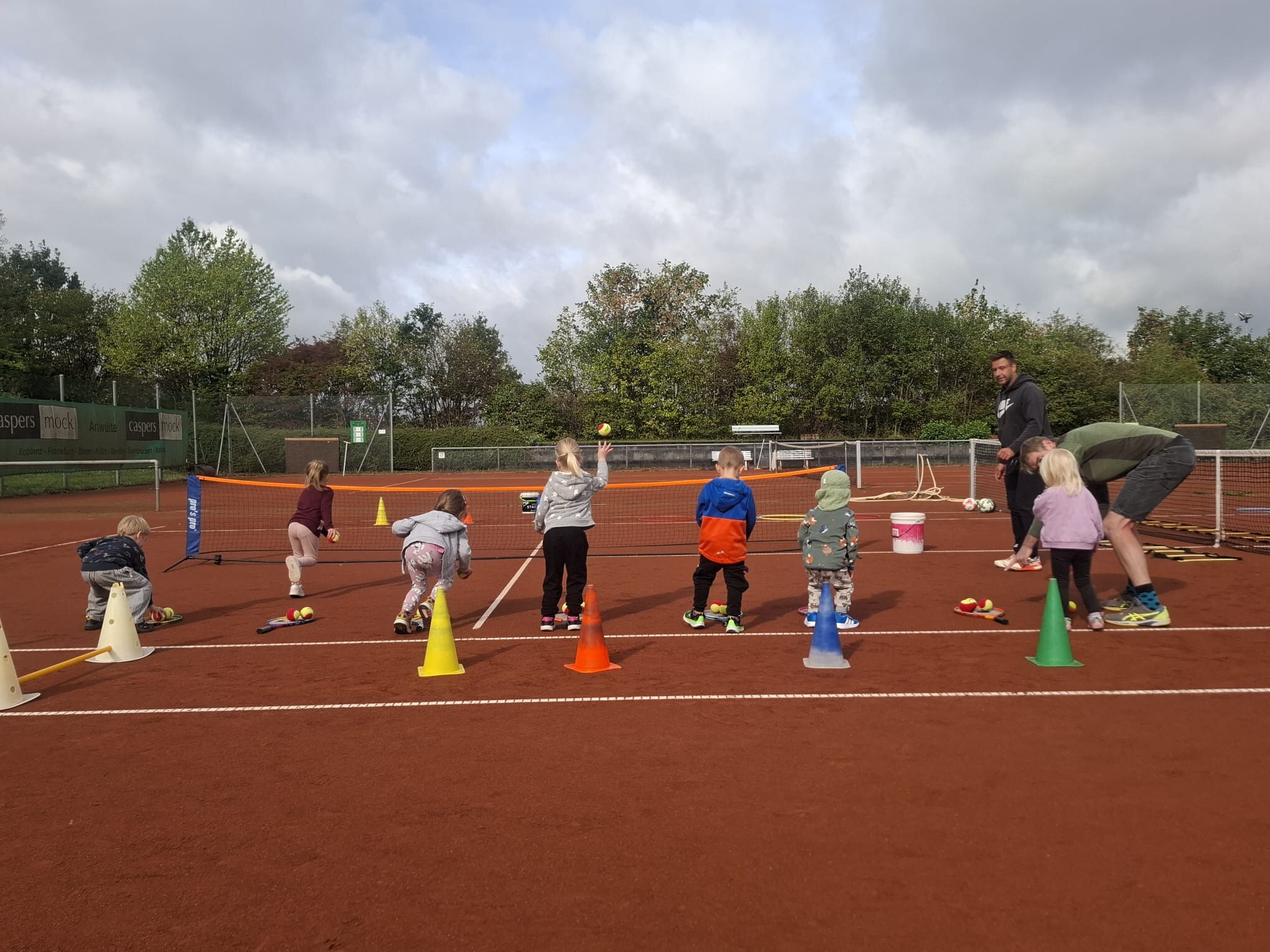 Kinder üben gemeinsam an verschiedenen Bewegungsstationen auf dem Tennisplatz